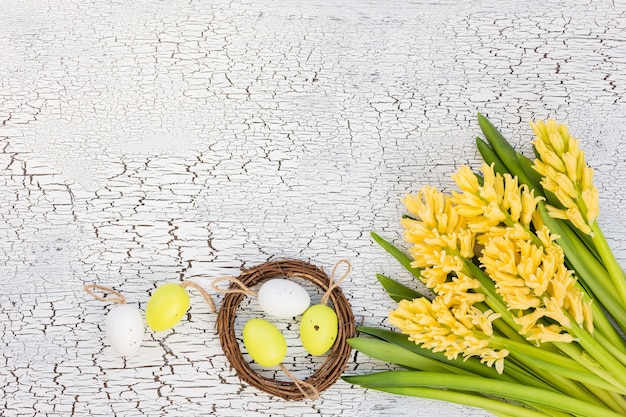 Osterhintergrund mit gelben Blumen und dekorativen Eiern im kleinen Nest. Draufsicht, Kopierraum