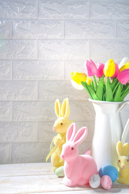 Osterhintergrund. Vase mit einem Blumenstrauß aus Tulpenblumen, Ostereiern und Hasendekor. Auf weißem Holz Küchentisch Hintergrund kopieren Raum