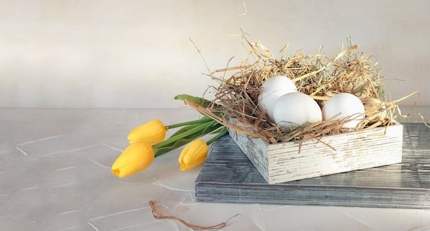 Osterkomposition mit frühlingsgelben Tulpenblumen und weißen Hühnereiern in Holzkiste