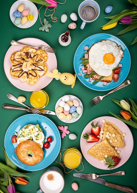 Osterkomposition mit Frühstücksebene lag mit Rührei-Bagels, Tulpen, Pfannkuchen, Brottoast mit Spiegelei und grünem Spargel, farbigen Wachteleiern. Draufsicht