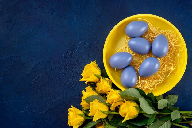 Osterkomposition mit gelben Rosen und Eiern auf dunkelblauem Hintergrund