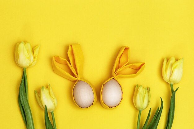 Osterkomposition mit handgemachtem buntem Osterei mit Ohren vom Kaninchen und Strauß der frischen gelben Blumen Tulpe