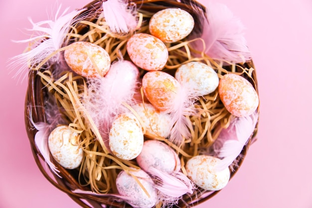 Osterkomposition mit traditionellem Dekor. Kleiner Deon rosa heller Hintergrund. Korative bunte Eier und weiche Federn in einem Weidenkorb
