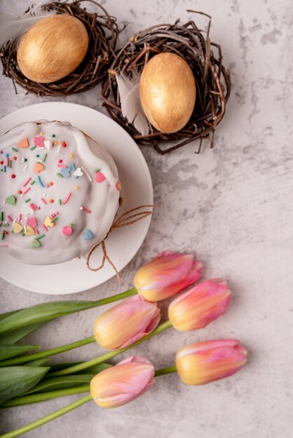 Osterkonzept. Glasierter Osterkuchen mit Tulpen und farbigen Eiern Draufsicht flach lag