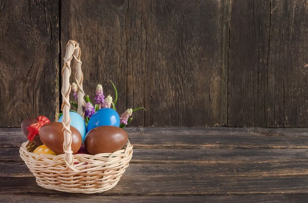 Osterkorb mit Schokoladeneiern mit Blumenstrauß der Frühlingsblumen auf Holztisch mit Kopienraum