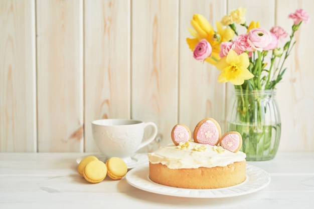Osterkuchen auf Tisch, Makronen, Eiern und Blumenstrauß in Vaseaster