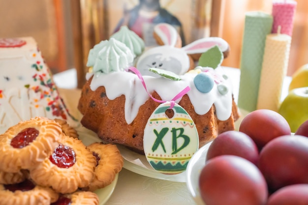 Osterkuchen mit bemalten Eiern, Äpfeln und Keksen auf dem Tisch in der Küche zu Hause Kirchenikonen und Kerze im Hintergrund Thema der orthodoxen Religion