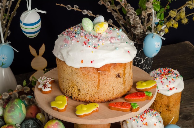 Osterkuchen und Eier auf einem festlichen Ostertisch mit Weide und einer Hasenfigur auf dunklem Hintergrund