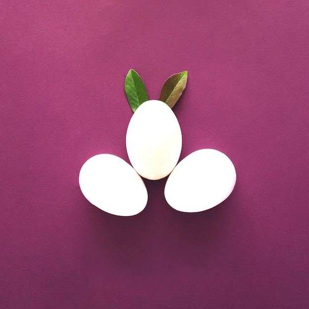Ostern drei weiße Eier mit grünen Blättern wie Hasenohren auf violettem Hintergrund