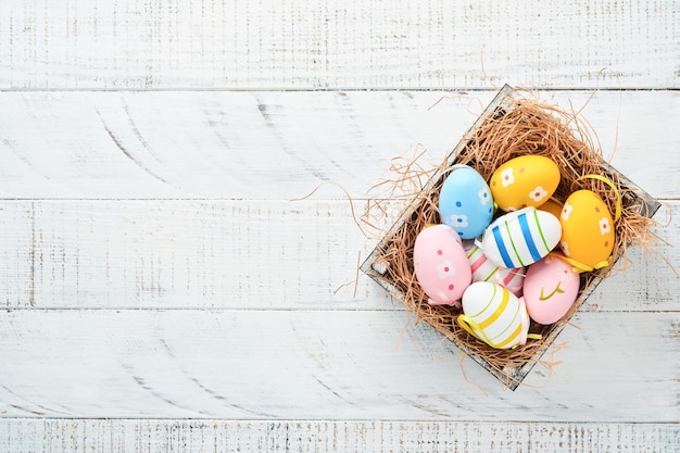 Ostern-Feiertag Bunte Ostereier im hölzernen Korb auf weißem hölzernem Hintergrund Ostern-Grußkarte Draufsichtkopienraum