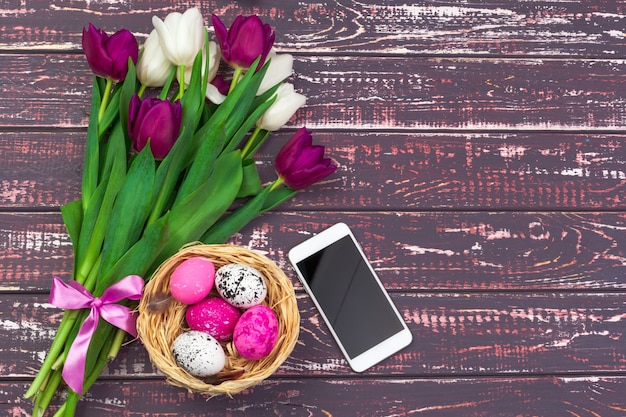 Ostern, Feiertage, Tradition und Gegenstandkonzept - nah oben von farbigen Ostereiern, von Tulpenblumen und von Smartphone auf hölzernem Hintergrund