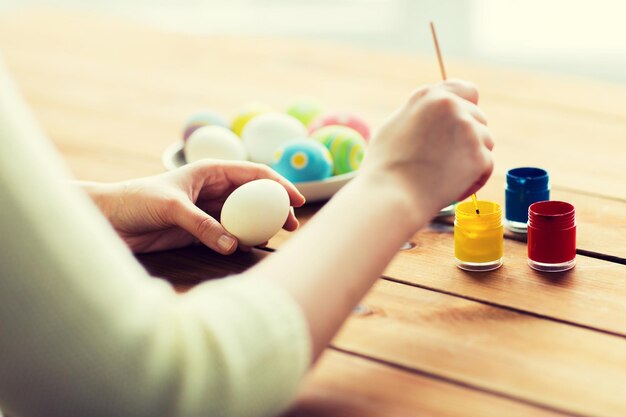 Foto ostern, feiertage, tradition und menschenkonzept - nahaufnahme einer frau, die ostereier mit farben und pinsel färbt