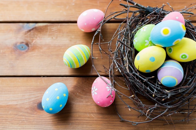 ostern, feiertage, tradition und objektkonzept - nahaufnahme farbiger ostereier im nest auf holzoberfläche