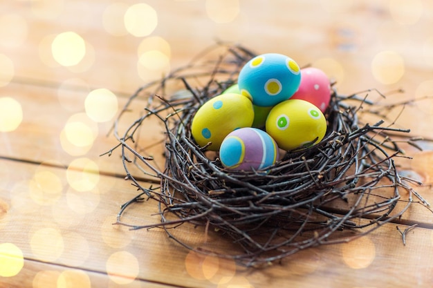 ostern, feiertage, tradition und objektkonzept - nahaufnahme farbiger ostereier im nest auf holzoberfläche