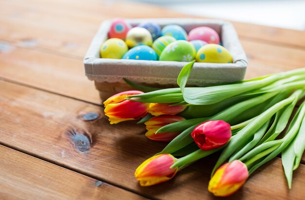 ostern, feiertage, tradition und objektkonzept - nahaufnahme von farbigen ostereiern im korb und tulpenblumen