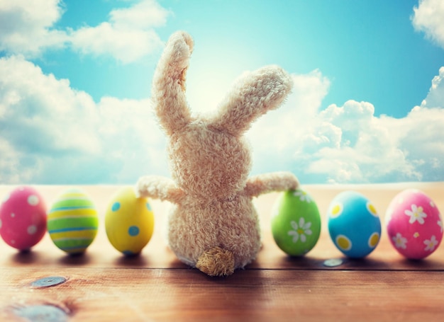 Ostern, Feiertage, Tradition und Objektkonzept - Nahaufnahme von farbigen Ostereiern und Kaninchen über blauem Himmel und Wolken im Hintergrund
