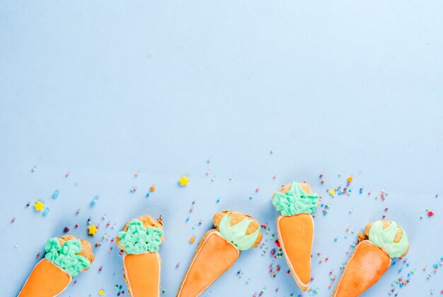 Ostern-Feiertagskonzept, süße Plätzchen in der Form von Karotten, Osterhase, mit Bonbon besprüht, hellblaue Draufsicht des Hintergrundkopienraumes, Grußkartenhintergrund