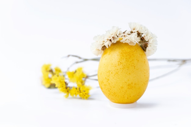 Ostern gelbes Ei mit Kranz und Wildblumen auf weißem Hintergrund