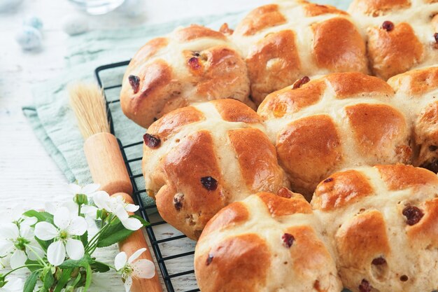 Ostern heiße Kreuzbrötchen Traditionelle Osternbrötchen mit Rosinen, Schokoladenbutter, Süßigkeiten, Eier mit blühenden Kirsch- oder Apfelblumen auf rustikalem hellen Holzhintergrund Osternessen