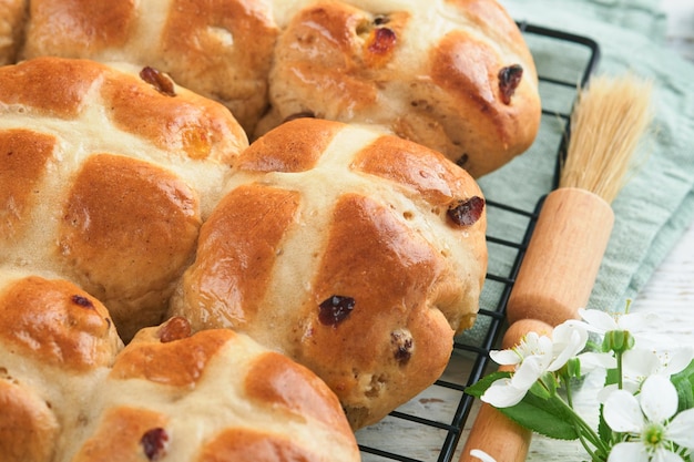 Ostern heiße Kreuzbrötchen Traditionelle Osternbrötchen mit Rosinen, Schokoladenbutter, Süßigkeiten, Eier mit blühenden Kirsch- oder Apfelblumen auf rustikalem hellen Holzhintergrund Osternessen