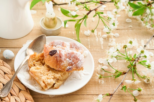 Ostern heiße Kreuzbrötchen Traditionelle Osternbrötchen mit Rosinen, Schokoladenbutter, Süßigkeiten, Eier mit blühenden Kirsch- oder Apfelblumen auf rustikalem hellen Holzhintergrund Osternessen