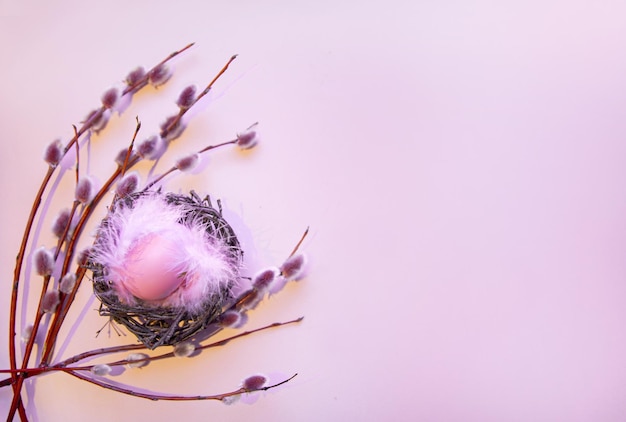 Ostern-Hintergrund mit bunten Eiern in einem Nest mit Weidenzweigen auf einem rosa Hintergrund mit Kopienraum-Grußkartenhintergrund