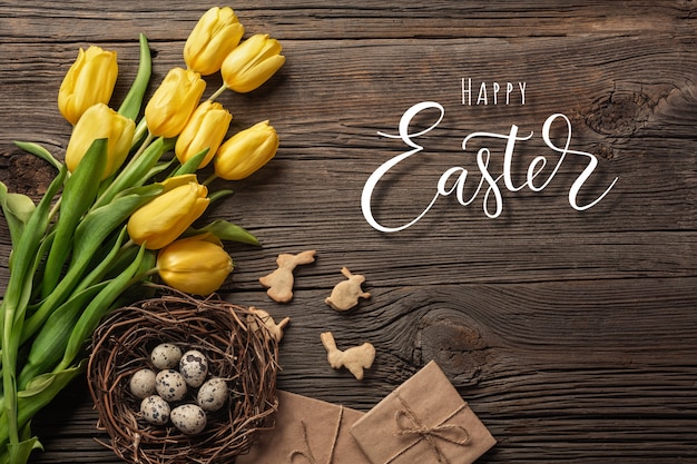 Ostern-Hintergrund mit bunten Eiern und gelben Tulpen auf Holztisch, Draufsicht