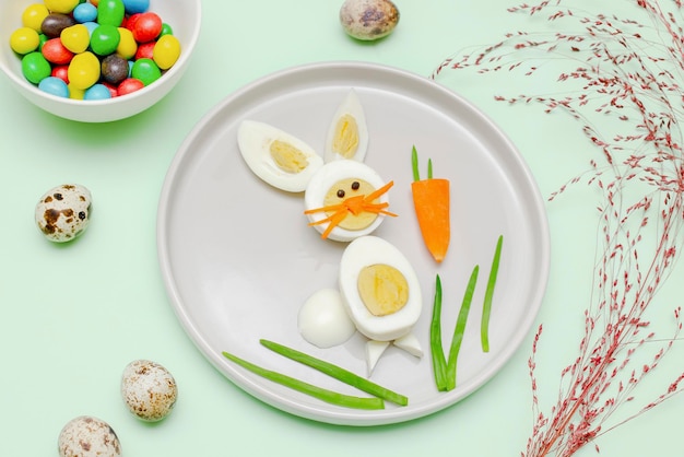 Ostern lustig kreative gesunde Frühstück Mittagessen Essen Idee für Kinder Kinder Hase aus gekochten Hühnereiern geschälte Karotten Grüns auf Platte grüner Tisch Hintergrund Ansicht von oben flach liegen
