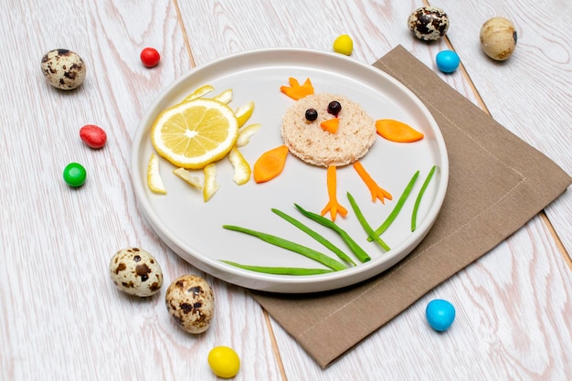 Ostern lustige kreative gesunde Frühstück Mittagessen Essen Idee für Kinder Kinder Sandwich in Hühnchenform aus Brot geschälte Karotten Grüns Gemüse auf Platte Holztisch Hintergrund Ansicht von oben Flach