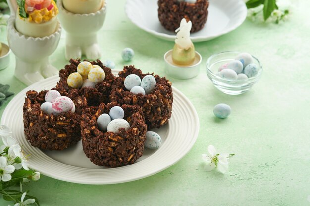 Ostern-Schokoladen-Nestkuchen mit Mini-Schokolade-Eiern mit blühenden Kirsch- oder Apfelblüten auf grünem Hintergrundtisch, kreatives Rezept für Ostertisch mit Feiertagsdekorationen, Draufsicht