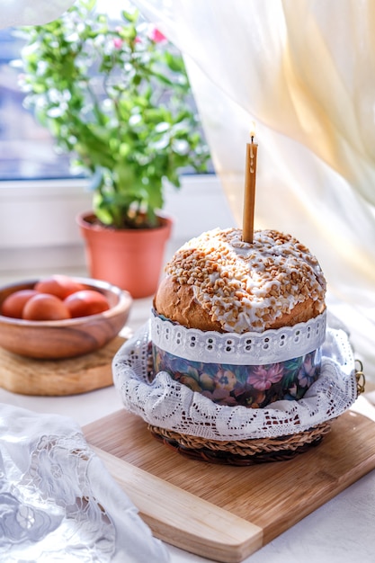 Ostern-Tabelle mit Osterkuchen und Ostereiern mit einem blühenden Zweig in einem Vase auf dem Tisch am Fenster