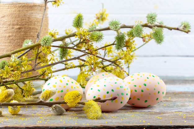 Ostern-Zusammensetzung von blühenden Weidenzweigen, von Hartriegeln und von Ostereiern mit einem Muster von gelben und grünen Punkten auf einer hölzernen Retro- Hintergrundraumnahaufnahme