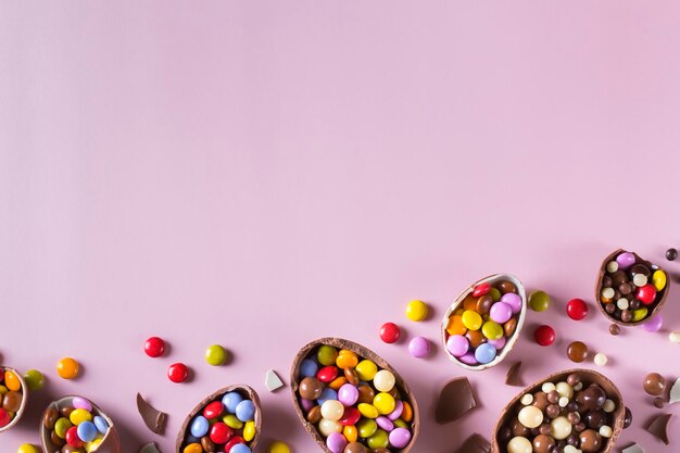 Osterrahmen mit Schokoladeneiern und Süßigkeiten auf rosa Hintergrund. Kopieren Sie Platz, Draufsicht, flache Lage