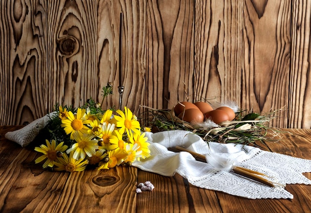 Osterstillleben Gelbe Gänseblümchen, Kerzen und Eier auf einem Holztisch in der Nähe