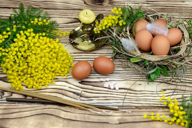 Osterstillleben Zweige von Mimosenkerzen und Eiern auf einem Holztisch in der Nähe