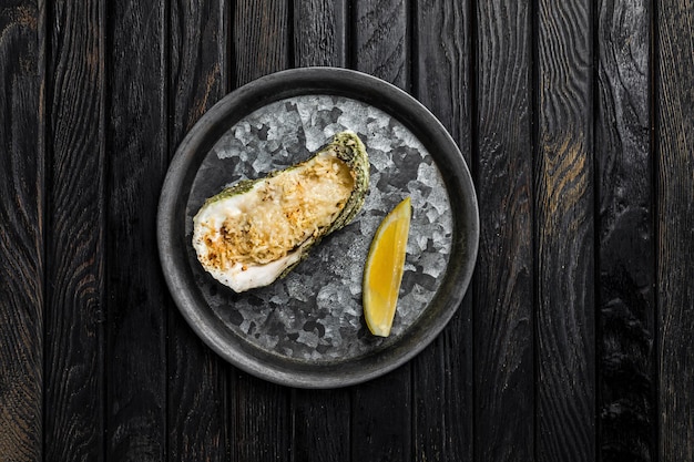 Ostra horneada con queso servida con limón en un plato metálico rústico rodado en la parte superior de la vista de fondo de madera