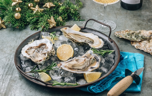 Ostras crudas abiertas con limón y romero. Mariscos frescos en una bandeja de metal. Concepto de navidad