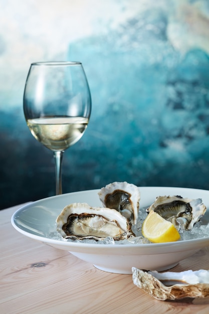 Ostras frescas con limón en un plato y una copa de vino en la mesa de madera