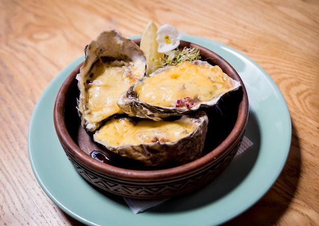 Ostras frescas bajo el queso en un plato con hielo y flores. Restaurante