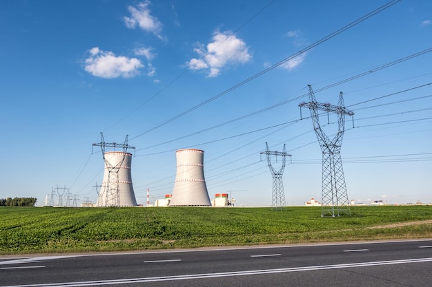 Foto ostrovec bielorrusia julio 2020 torres de refrigeración de la planta de energía nuclear con torres de pilones eléctricos de alto voltaje contra el cielo azul