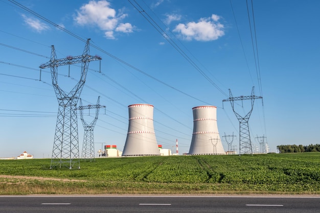 Foto ostrovec bielorrusia julio 2020 torres de refrigeración de la planta de energía nuclear con torres de pilones eléctricos de alto voltaje contra el cielo azul