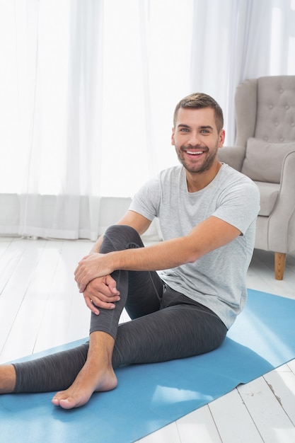 Ótimo humor. homem alegre e positivo sorrindo enquanto está sentado em uma esteira de ioga