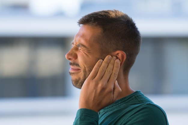 Otitis o tinnitus. Hombre tocándose la oreja debido a un fuerte dolor de oído o dolor de oído. . Foto de alta calidad