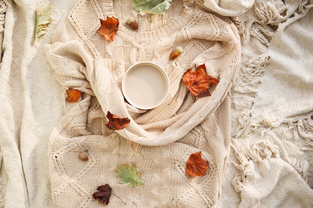 Otoño calido. Taza de café envuelta en un suéter beige de lana. naturaleza muerta.