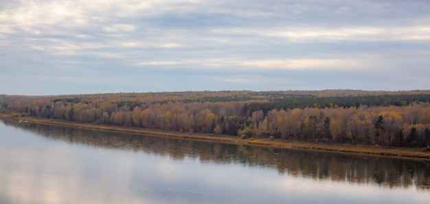 Otoño hermoso y ancho río entre los bosques. Lugar tranquilo y silencioso con colores otoñales. En medio de la isla fluvial. Vista desde arriba a la distancia