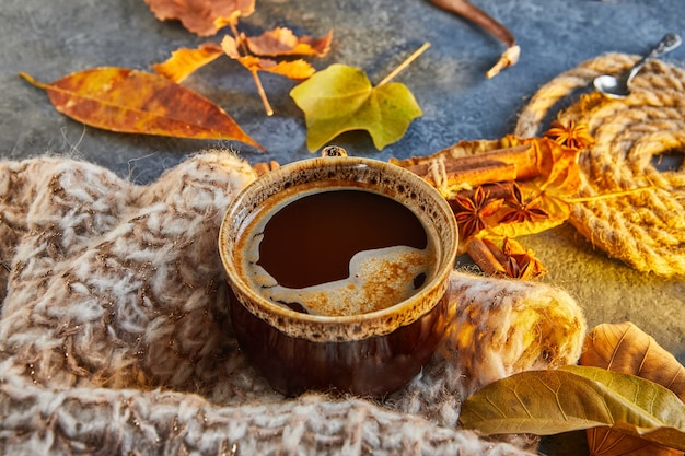 Otoño, hojas de otoño, una taza de café humeante y una bufanda caliente contra el fondo