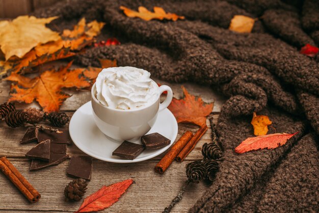 Otoño, hojas de otoño, taza de café humeante y una bufanda caliente en la mesa de madera.