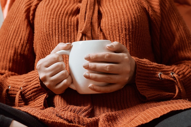 Otoño humor mujer joven en jersey de lana naranja bebiendo café refrescante en una fría mañana otoñal ...