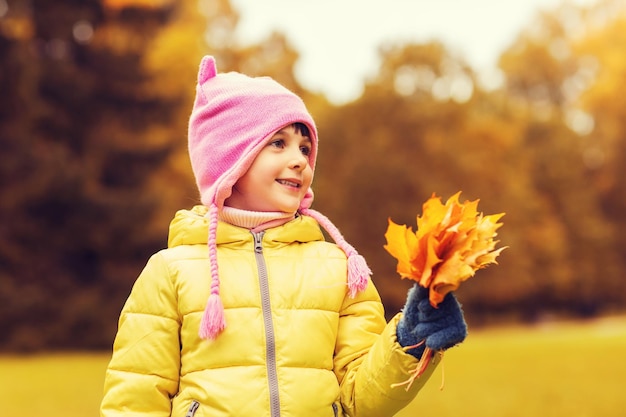 otoño, infancia, felicidad y concepto de la gente - niña feliz y hermosa con un montón de hojas de arce al aire libre