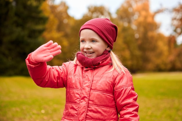 otoño, infancia, gesto, naturaleza y concepto de la gente - niña feliz saludando con la mano en el parque